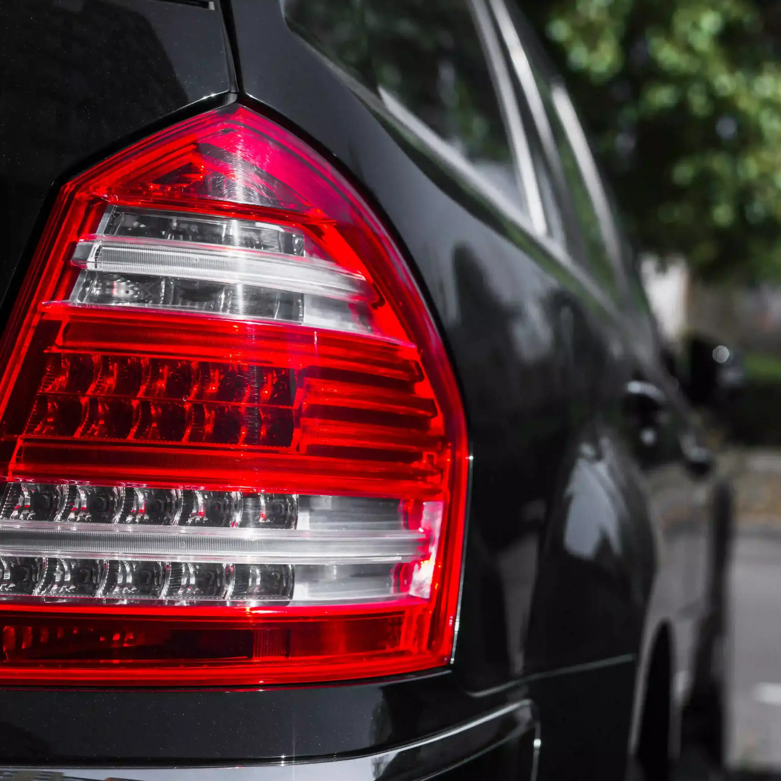 Close-up of a black car's rear taillight with red-and-clear LED design, highlighting sleek automotive styling and detail